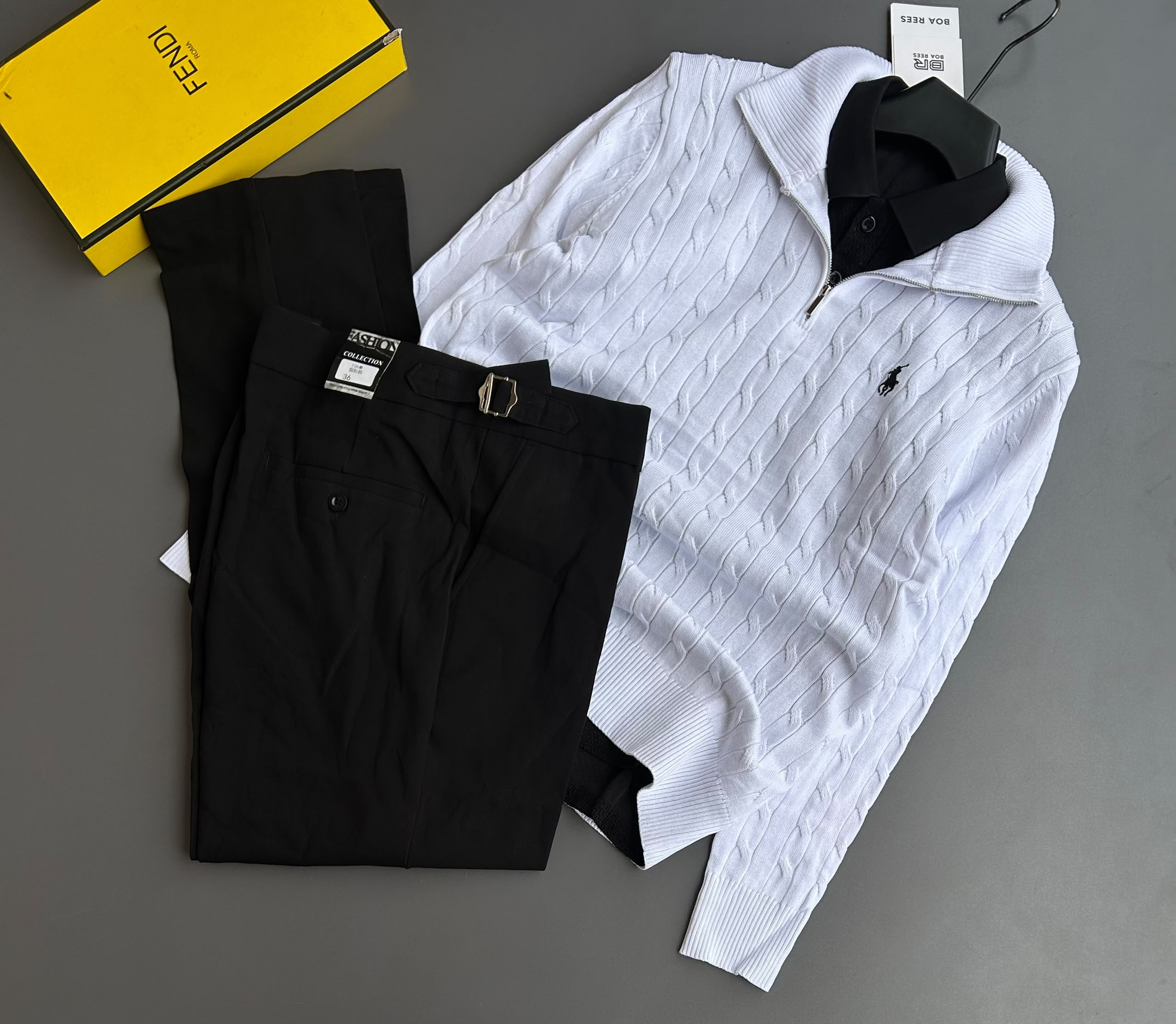 A cable-knit quarter-zip sweater featuring signature logo embroidery, paired with tailored black trousers with side-buckle waist adjusters.