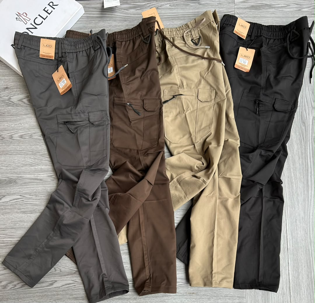 Elasticated drawstring waistband, multiple storage pockets (including zippered and flap-secured thigh cargo pockets), durable cotton-blend fabric, and reinforced knee stitching for utility or outdoor wear.