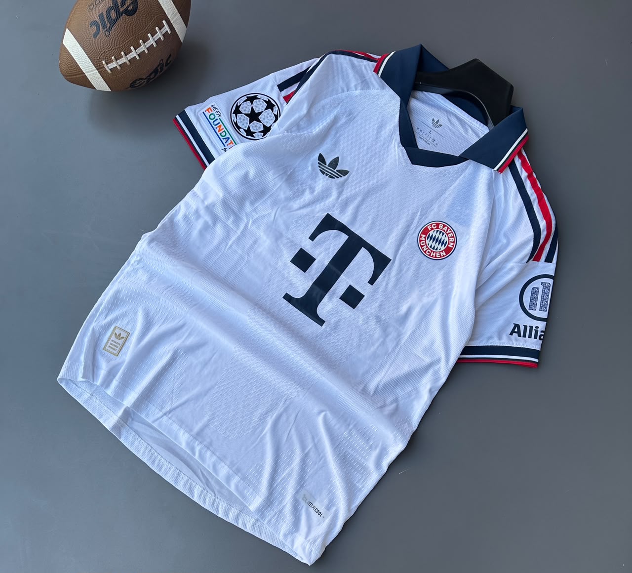 Polo-style v-neck collar, embroidered Adidas Trefoil logo, classic FC Bayern Munich crest, front "T" sponsor logo, UEFA Champions League and Foundation sleeve badges, and Allianz sleeve sponsor logo.