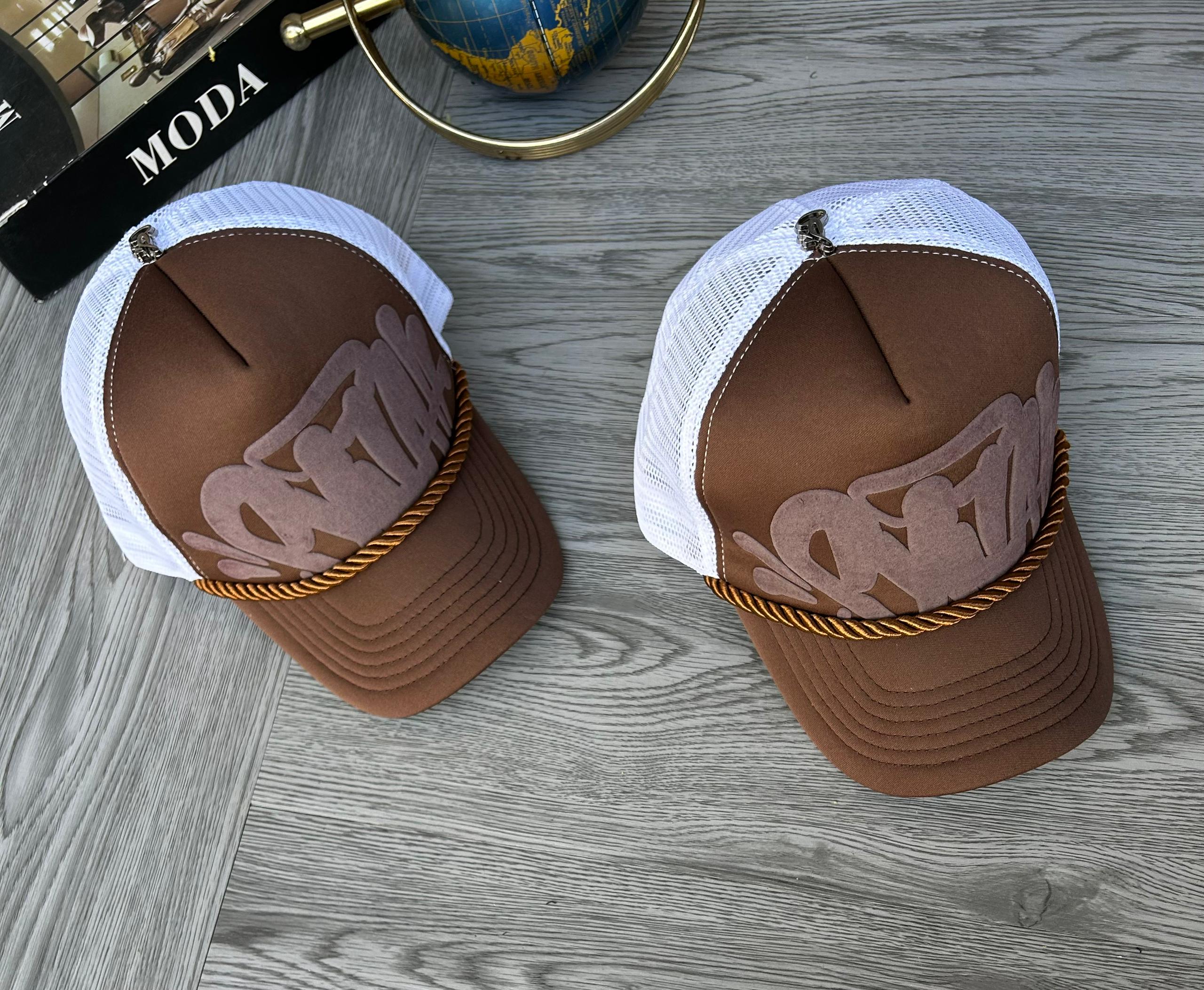 front crown with a plush suede graphic logo appliqué, breathable white mesh back paneling, a bronze-toned braided accent cord across the visor seam, and a top silver emblem embellishment.